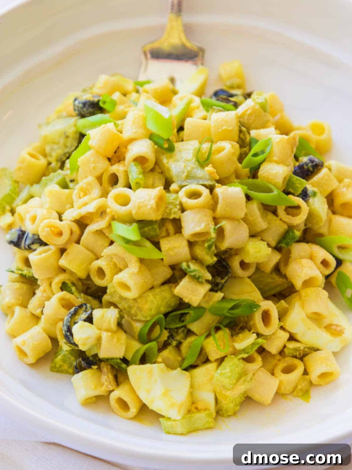 A white plate generously piled with homemade classic macaroni salad, showcasing its creamy texture and colorful ingredients.