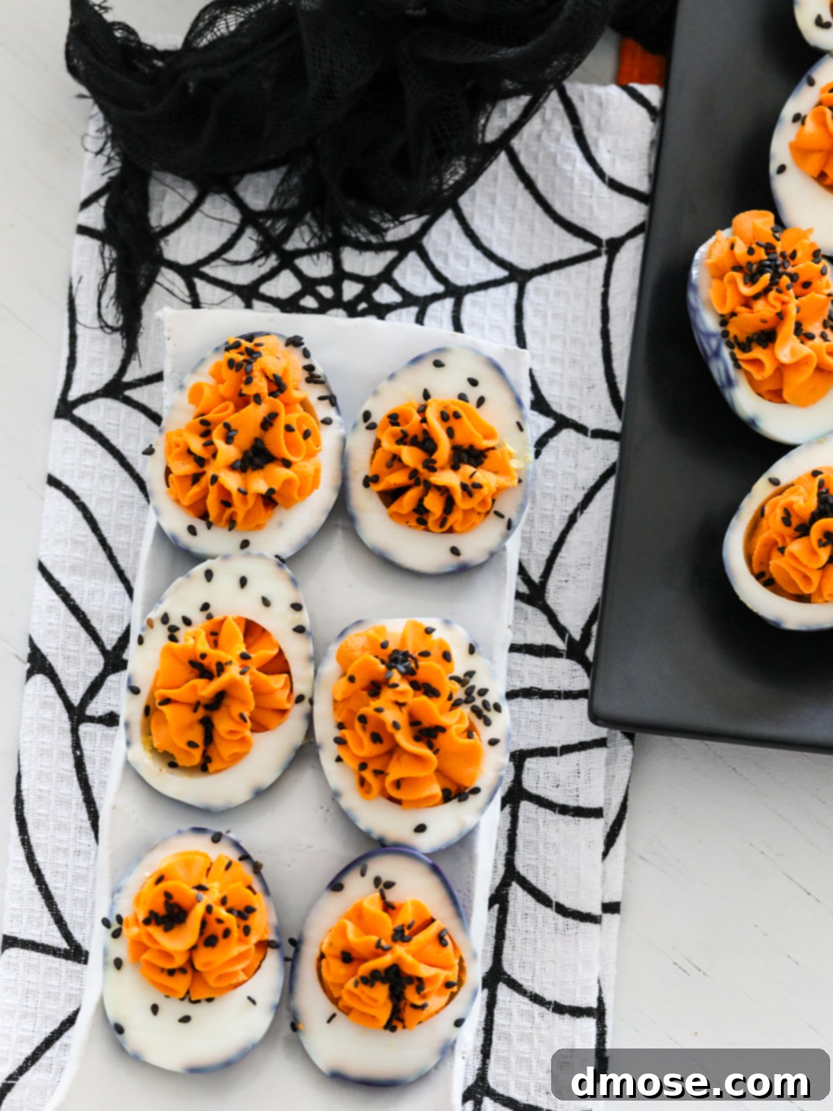 A white ceramic plate holding six Halloween deviled eggs, presented on a black and white spider tablecloth at a Halloween party.