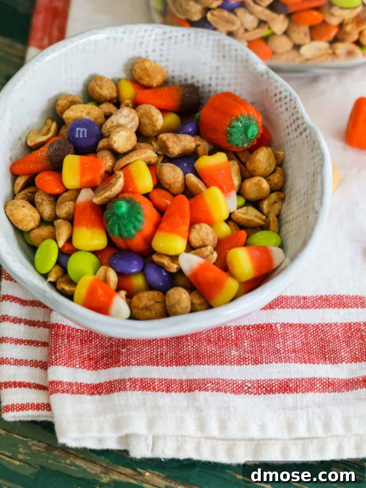 A small white ceramic bowl containing a vibrant Fall Snack Mix, highlighting the various colors and textures of candy and peanuts.