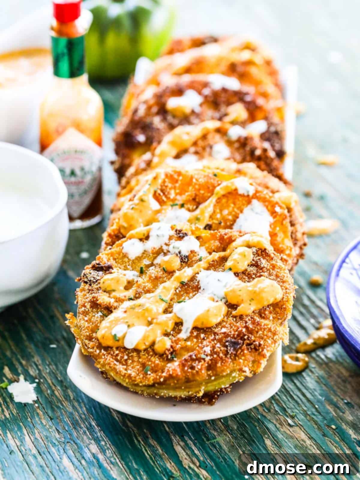 A stack of golden brown fried green tomatoes with small bowls of remoulade and buttermilk ranch dressing on a long white plate.