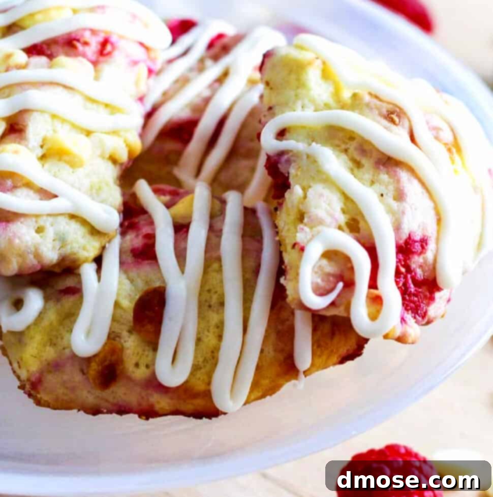 Small white cake plate with homemade raspberry scones studded with white chocolate chips and sweet red raspberries.