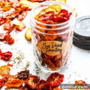 A small clear jar filled with sun dried tomatoes on a table with scattered dried tomatoes all around the table.