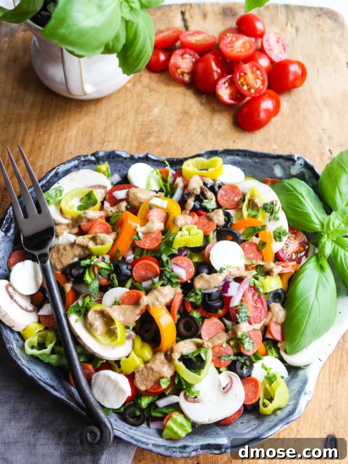 A close-up of a chopped Pizza Salad on a ceramic plate with a fork, showing the texture and freshness of the ingredients.
