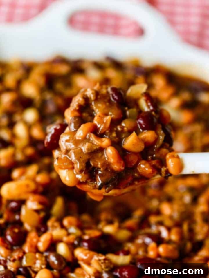 A large dish of cowboy beans with white spoon scooping out a serving.