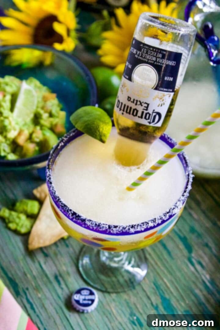 A large blue rimmed margarita glass with straw, lime, and Coronita beer poured inside the glass.