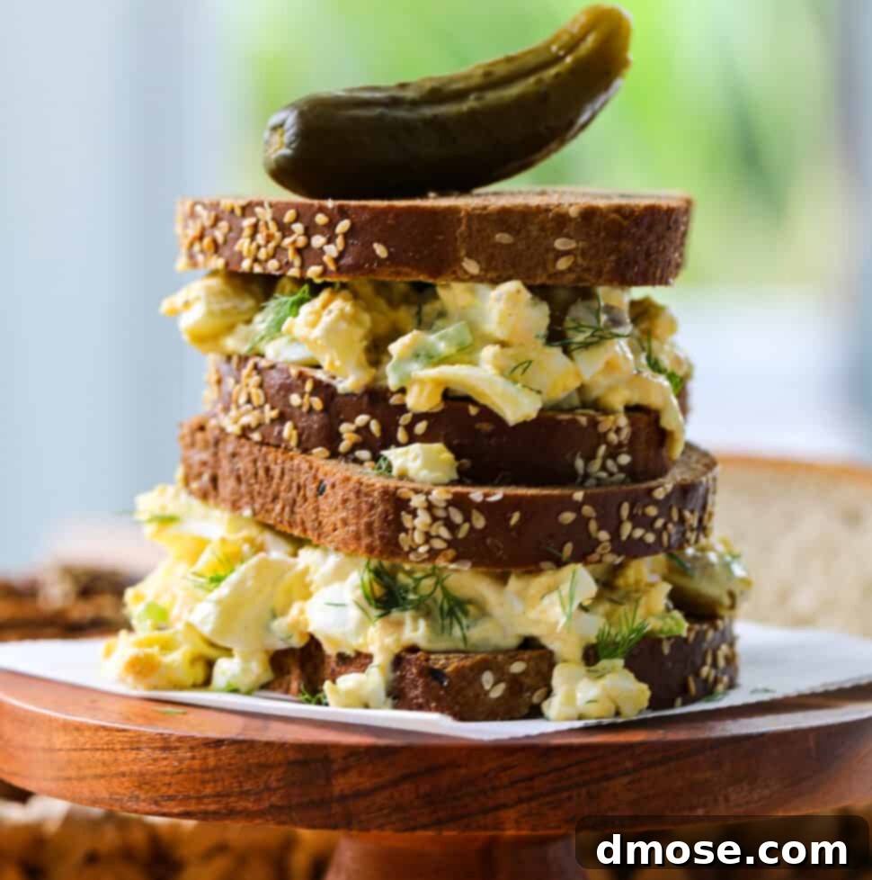 Savory Egg Salad Sensation 16 An egg salad sandwich on brown bread stacked on a wood stand with a pickle on top.