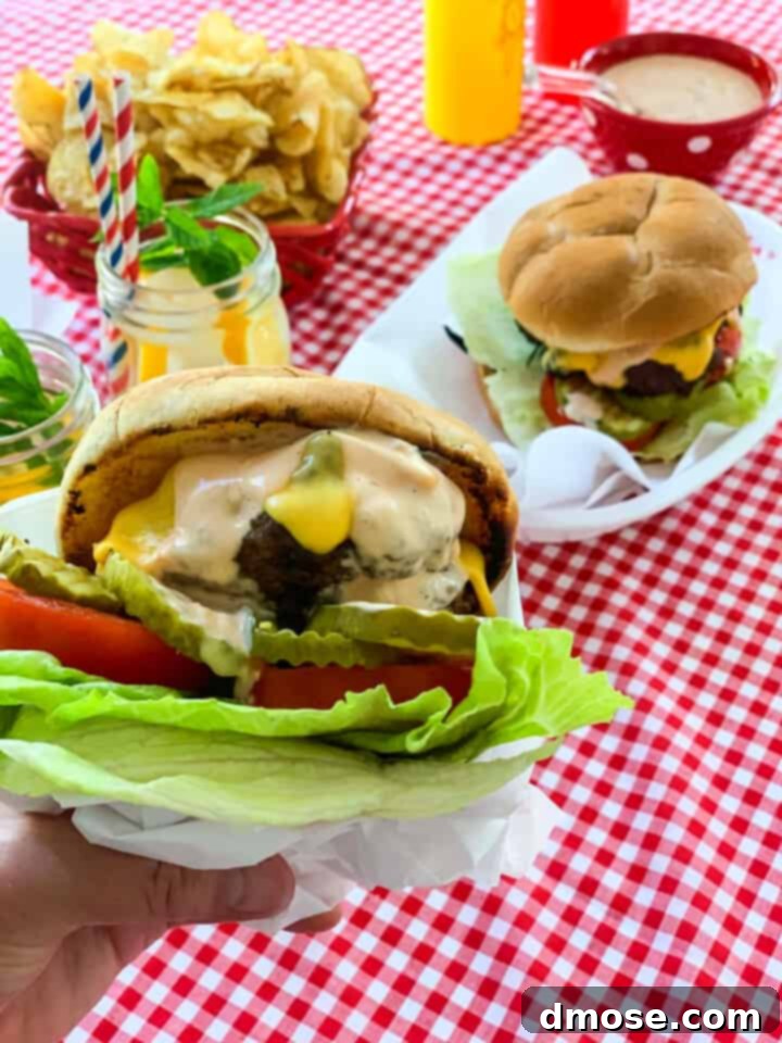 Graduation Party Food Inspiration for 2024 13 A lady holding a messy grilled hamburger wrapped in paper with baskets of burgers in the background.
