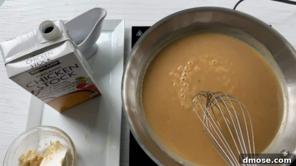 Savory Turkey Gravy 10 A hand continuously stirring turkey gravy with a wire whisk in a saucepan, ensuring a smooth consistency.