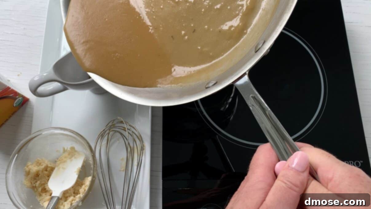 Savory Turkey Gravy 12 A hand pouring warm, golden turkey gravy from a saucepan into a elegant white gravy boat.