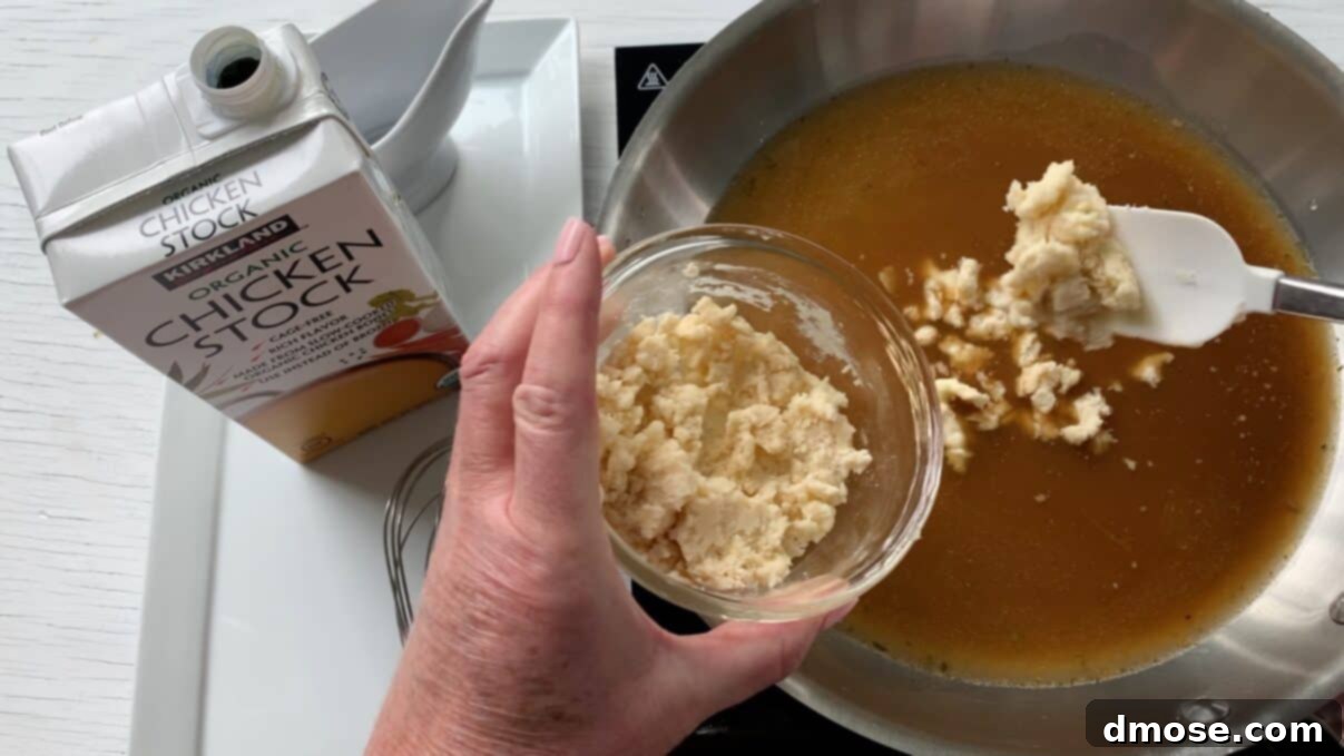 Savory Turkey Gravy 8 A hand adding a spoonful of the flour-butter mixture (Beurre Manié) into the simmering turkey drippings and chicken stock in a saucepan.