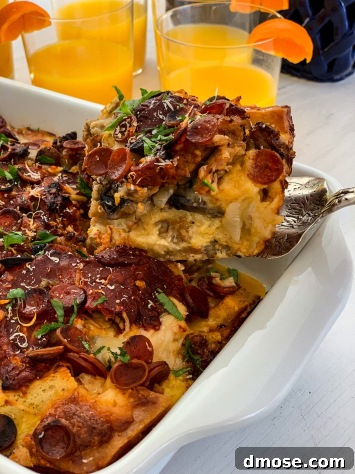 Cheesy Pizza Breakfast Bake 17 A hand lifting a slice of baked breakfast casserole with a spatula for brunch.