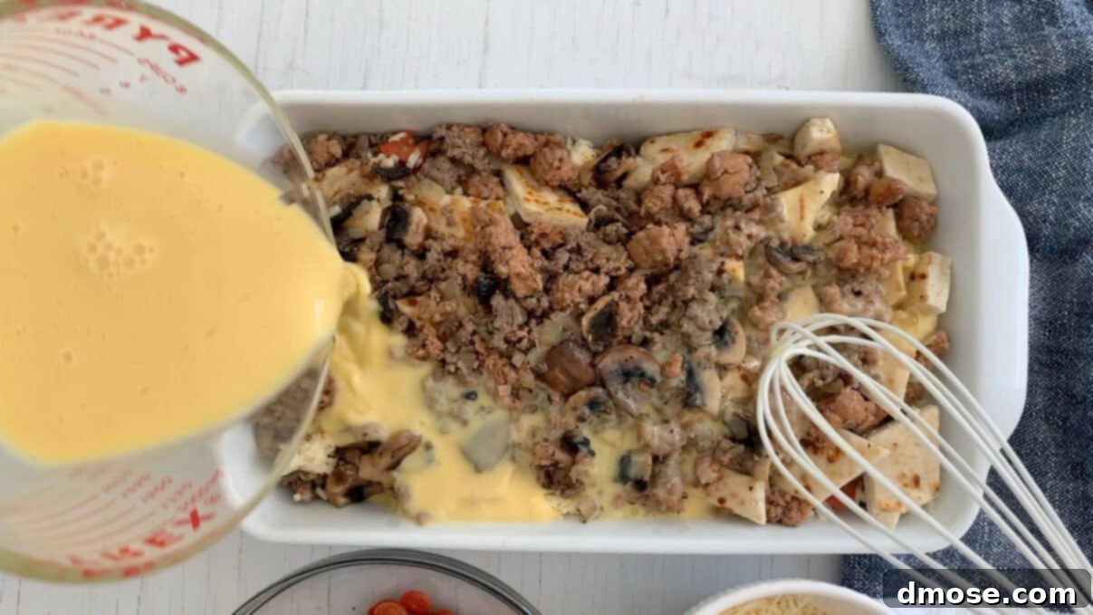 Cheesy Pizza Breakfast Bake 9 Pouring the egg and milk mixture over the assembled pizza breakfast casserole in a dish.