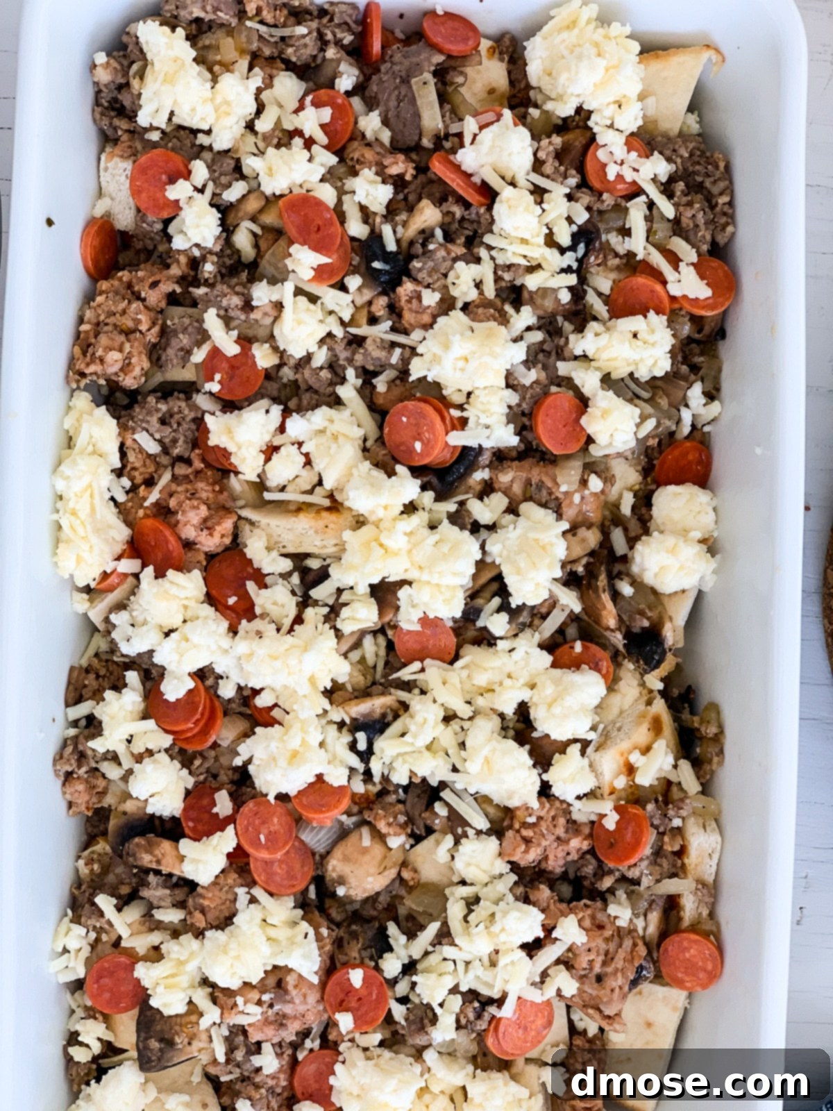 Cheesy Pizza Breakfast Bake 10 Assembling the final layers of the breakfast casserole with toppings in a white baking dish.