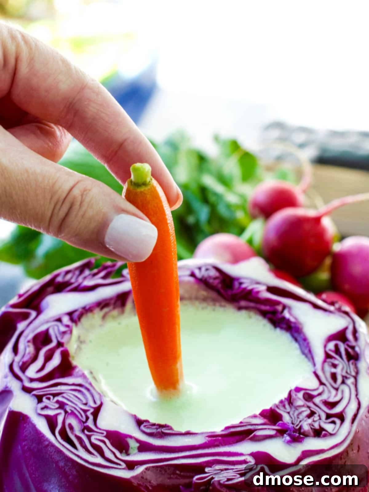 Colorful Veggies & Zesty Dip 7 A carrot stick being dipped into a creamy Green Goddess Dip in a purple cabbage bowl on a crudités platter.